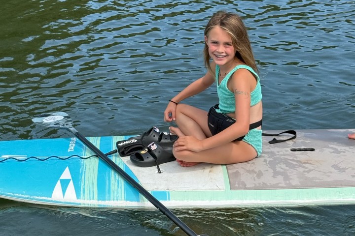 Girl sitting on a paddleboard in calm water, smiling.