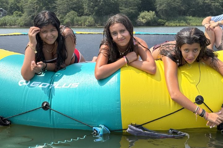 Three people on a floating inflatable water toy in a lake.