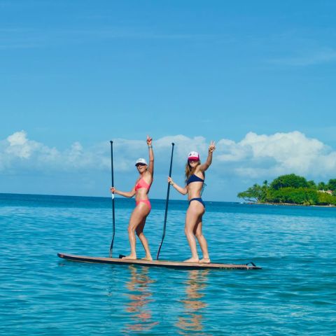Two women paddleboarding on clear blue ocean with an island in the background.