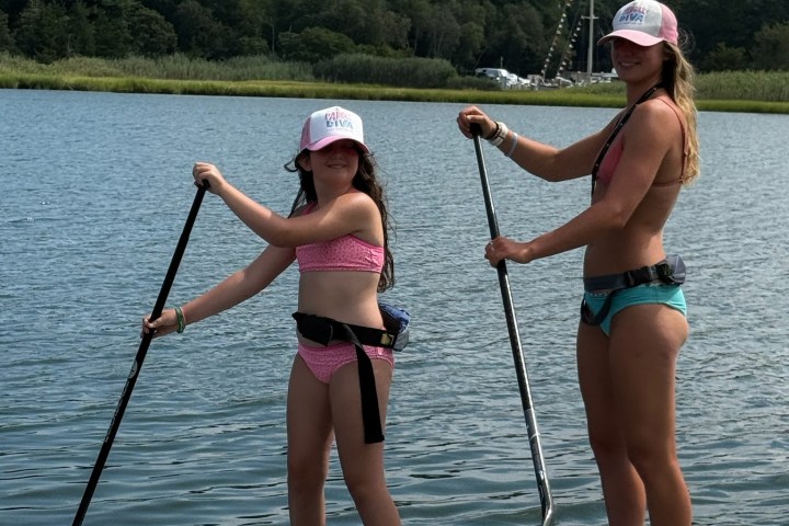 Two people paddleboarding on a calm lake with lush trees in the background.